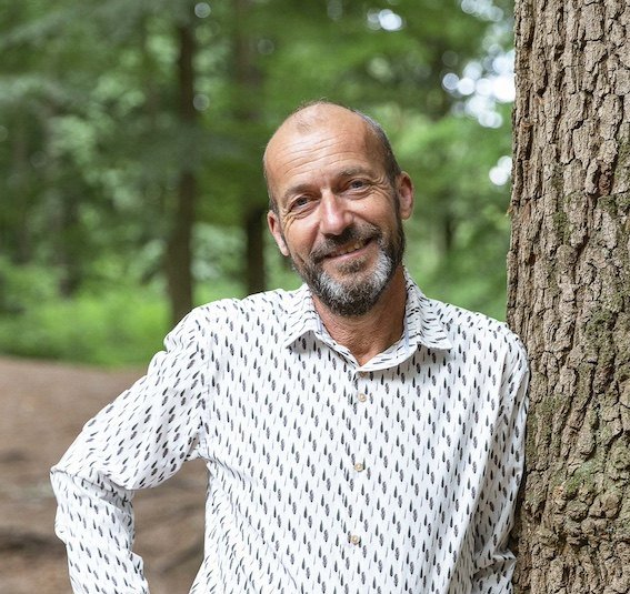 Reinier van den Berg, meteoroloog en spreker, leunend tegen een boom in het bos